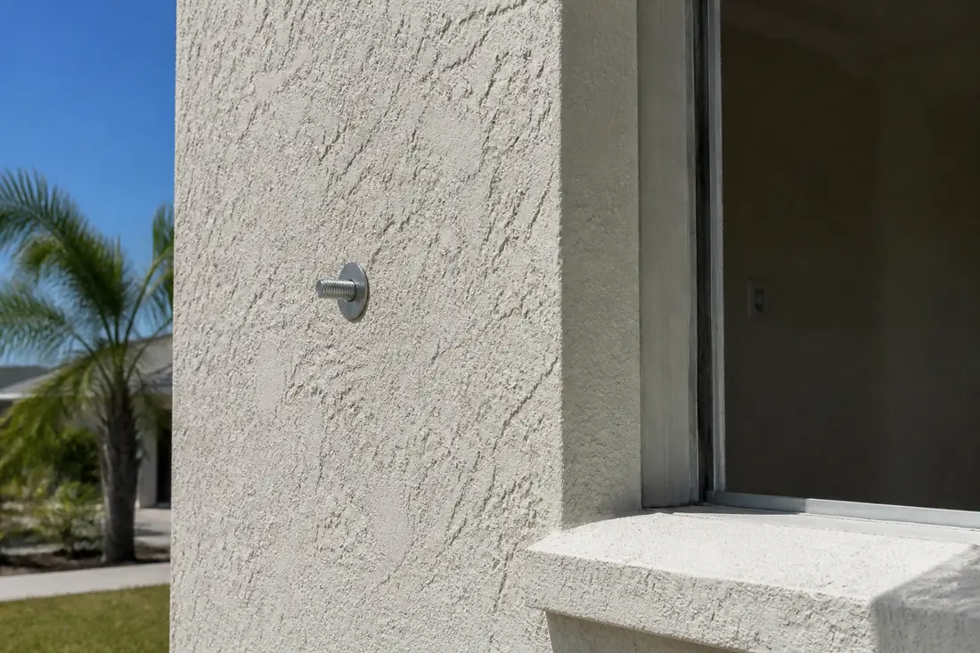 A permanently installed shutter anchor set into a stucco wall beside a window opening