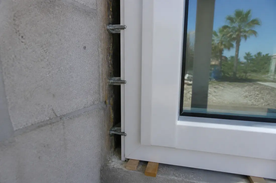 A line of masonry anchors through a window frame flange into a concrete block opening