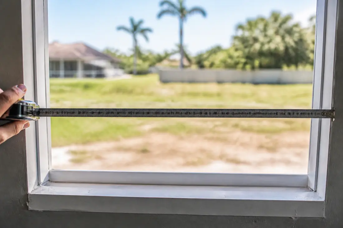 A steel tape measure held across the width of a window opening from the inside