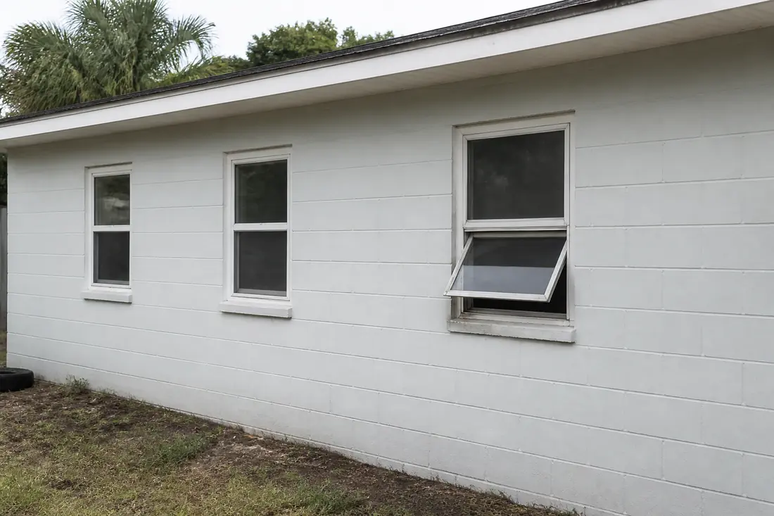 Three old aluminum single-hung windows on the side wall of an older Florida house