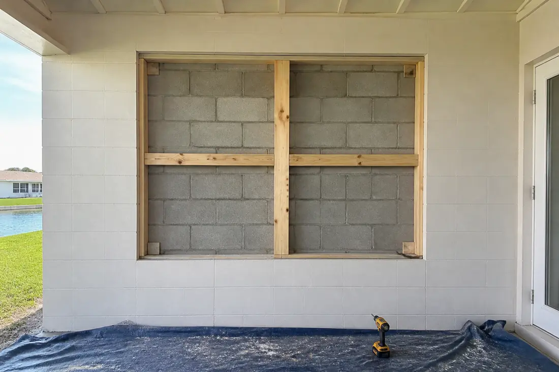 An empty window opening in a concrete block wall with the wood buck still in place